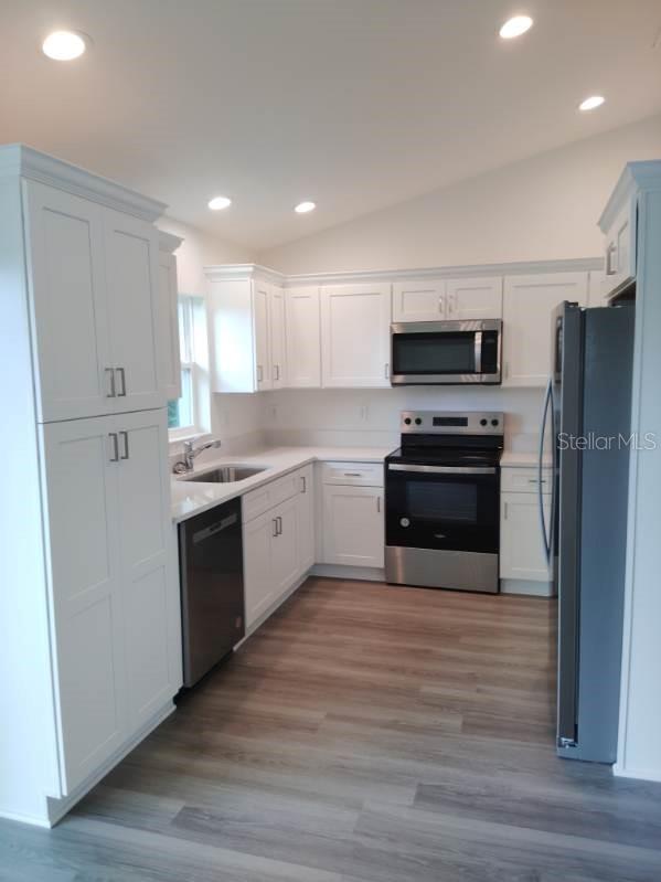 kitchen with white cabinets, sink, vaulted ceiling, stainless steel appliances, and light hardwood / wood-style floors