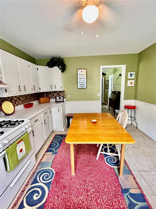 kitchen featuring gas range gas stove, tasteful backsplash, white cabinets, light tile patterned floors, and ceiling fan