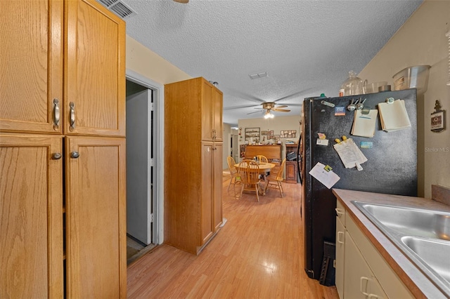 kitchen with light hardwood / wood-style floors, a textured ceiling, ceiling fan, refrigerator, and sink