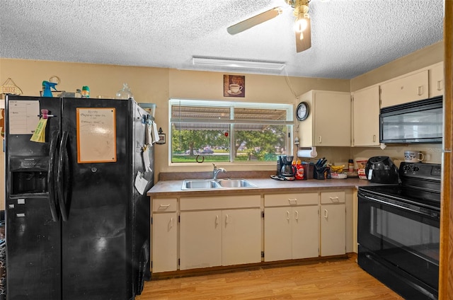 kitchen featuring a textured ceiling, light hardwood / wood-style floors, sink, cream cabinetry, and black appliances