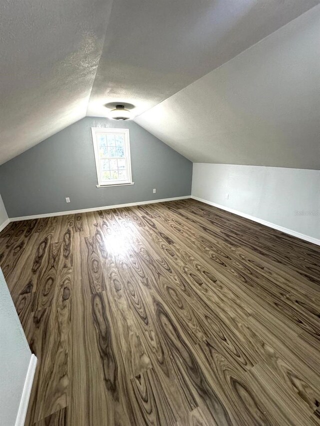 additional living space with lofted ceiling, a textured ceiling, and hardwood / wood-style flooring