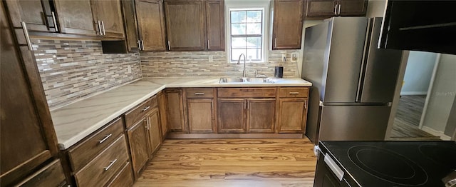 kitchen with light stone counters, sink, light hardwood / wood-style flooring, stainless steel refrigerator, and decorative backsplash