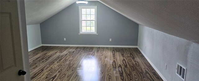 additional living space with lofted ceiling, a textured ceiling, and dark hardwood / wood-style flooring