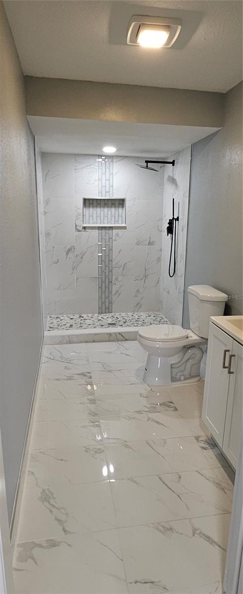 bathroom featuring a tile shower, vanity, and toilet