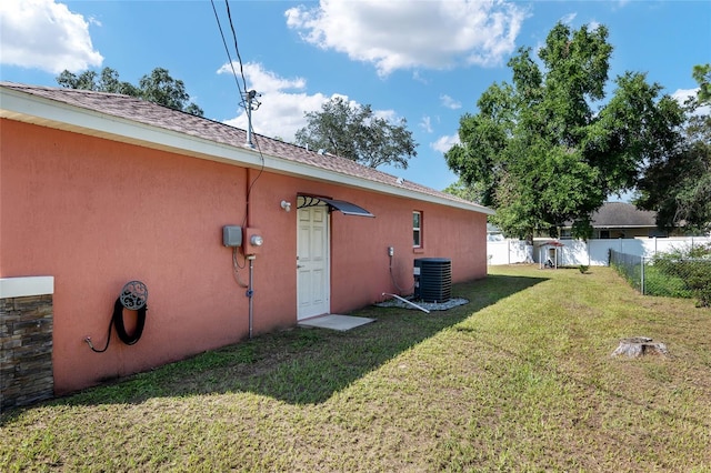 rear view of property with central AC unit and a lawn