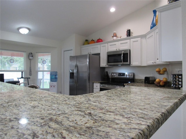 kitchen with white cabinetry, light stone countertops, kitchen peninsula, vaulted ceiling, and appliances with stainless steel finishes