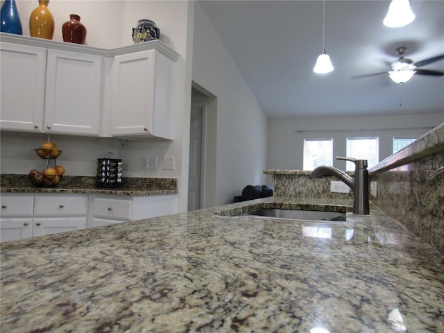 kitchen featuring lofted ceiling, stone counters, white cabinets, sink, and hanging light fixtures