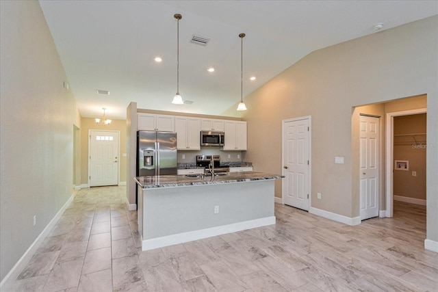 kitchen with appliances with stainless steel finishes, hanging light fixtures, white cabinetry, dark stone countertops, and a center island with sink