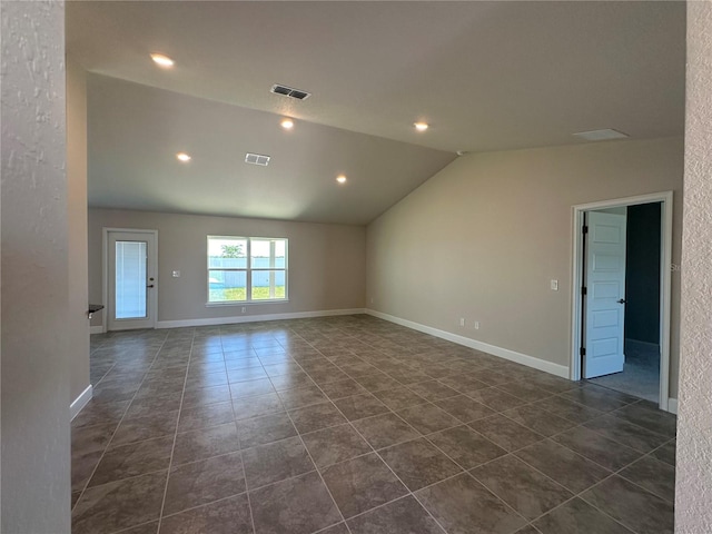 empty room featuring vaulted ceiling and dark tile patterned floors