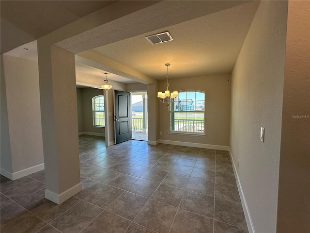 empty room featuring dark tile patterned flooring, a chandelier, and plenty of natural light