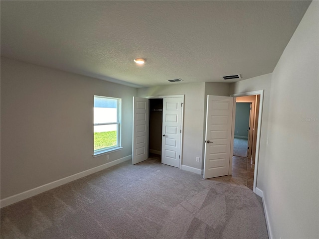 unfurnished bedroom featuring light colored carpet, a textured ceiling, and a closet