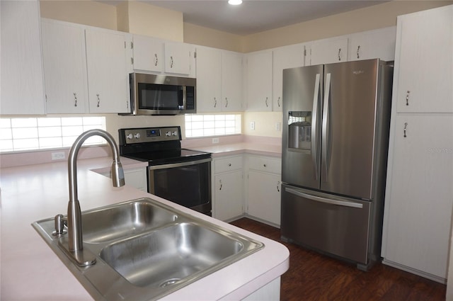 kitchen with appliances with stainless steel finishes, white cabinetry, dark hardwood / wood-style flooring, and sink