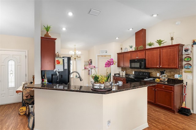 kitchen featuring lofted ceiling, black appliances, light hardwood / wood-style floors, and dark stone countertops