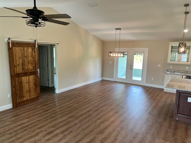 unfurnished living room with ceiling fan, vaulted ceiling, dark hardwood / wood-style floors, and a barn door