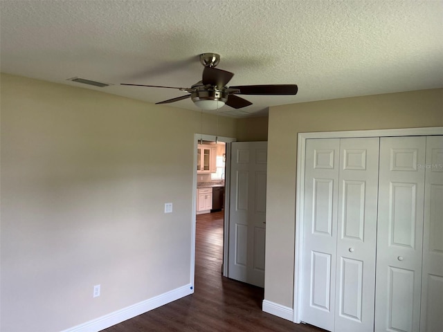 unfurnished bedroom with a textured ceiling, dark hardwood / wood-style flooring, ceiling fan, and a closet