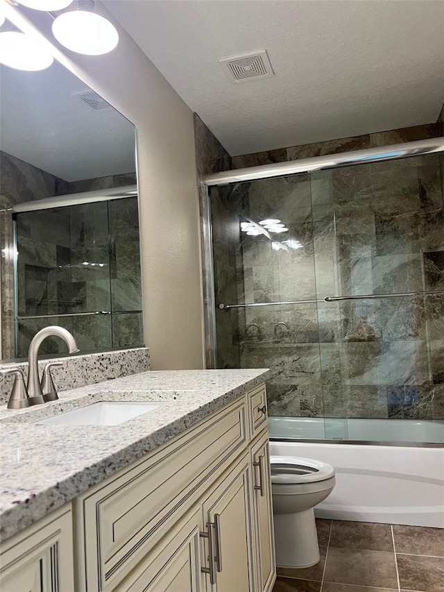 full bathroom with vanity, a textured ceiling, tile patterned flooring, bath / shower combo with glass door, and toilet