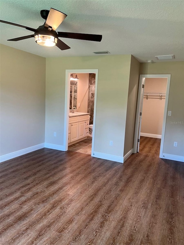 unfurnished bedroom with a closet, a textured ceiling, dark wood-type flooring, a spacious closet, and ceiling fan