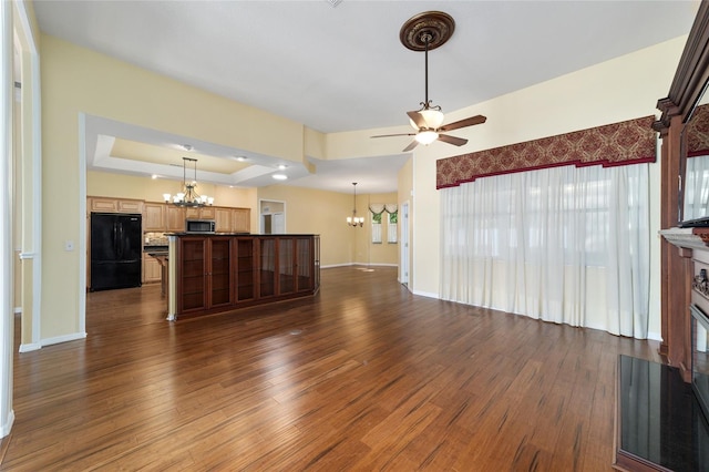 unfurnished living room with ceiling fan with notable chandelier, dark hardwood / wood-style floors, and a tray ceiling