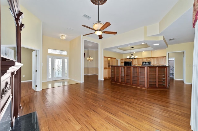 unfurnished living room with light wood-type flooring, ceiling fan with notable chandelier, a high end fireplace, and a raised ceiling