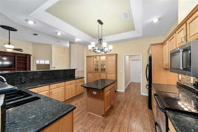 kitchen with pendant lighting, a tray ceiling, ceiling fan with notable chandelier, a kitchen island, and black appliances