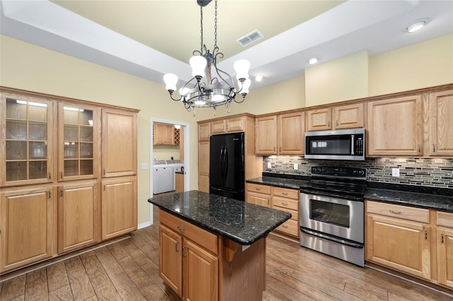 kitchen with a chandelier, appliances with stainless steel finishes, washing machine and dryer, a center island, and hardwood / wood-style floors