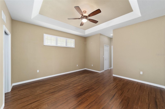 empty room with a raised ceiling, dark wood-type flooring, and ceiling fan