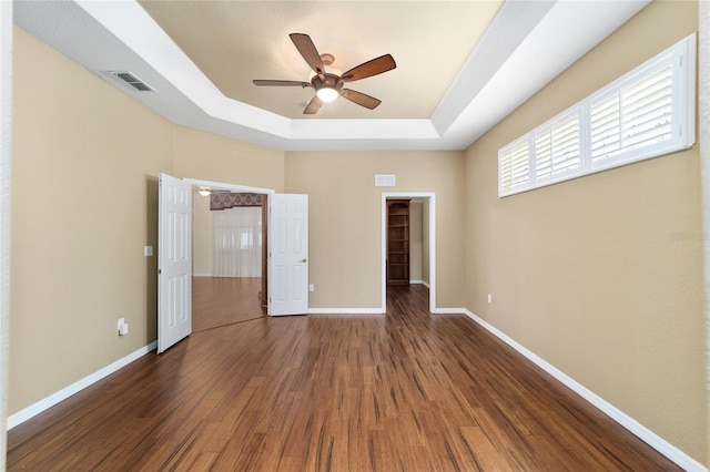 unfurnished bedroom featuring a tray ceiling, ceiling fan, dark wood-type flooring, and a walk in closet