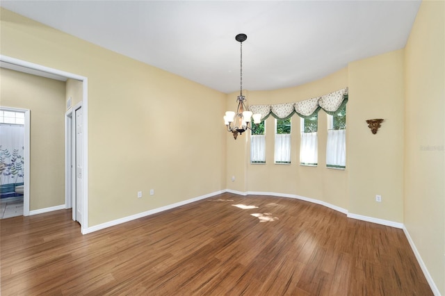 empty room featuring wood-type flooring and an inviting chandelier