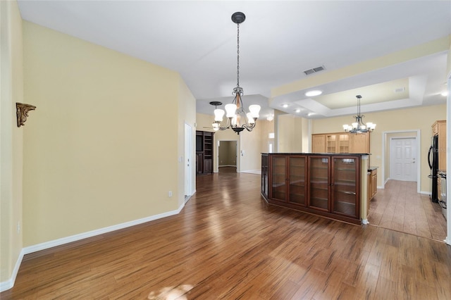 interior space featuring an inviting chandelier, a tray ceiling, and dark hardwood / wood-style flooring