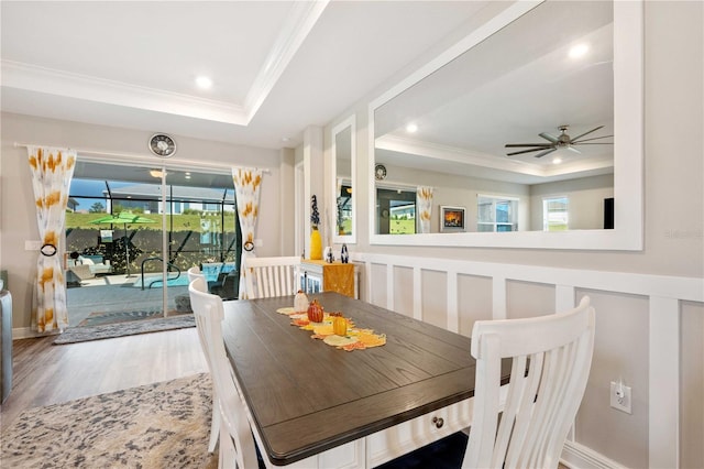 dining space featuring wood-type flooring, a tray ceiling, ceiling fan, and crown molding