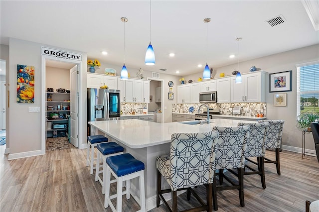 kitchen with light hardwood / wood-style floors, pendant lighting, stainless steel appliances, and white cabinets