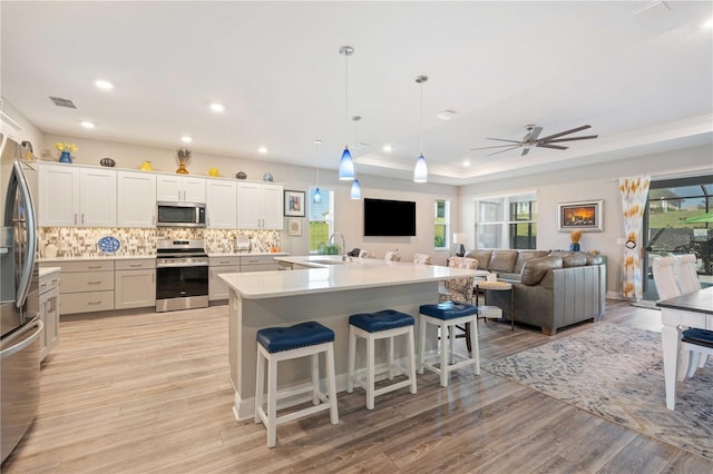 kitchen with white cabinetry, hanging light fixtures, light hardwood / wood-style flooring, appliances with stainless steel finishes, and ceiling fan