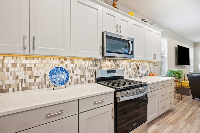 kitchen with white cabinetry, light hardwood / wood-style flooring, decorative backsplash, appliances with stainless steel finishes, and light stone countertops