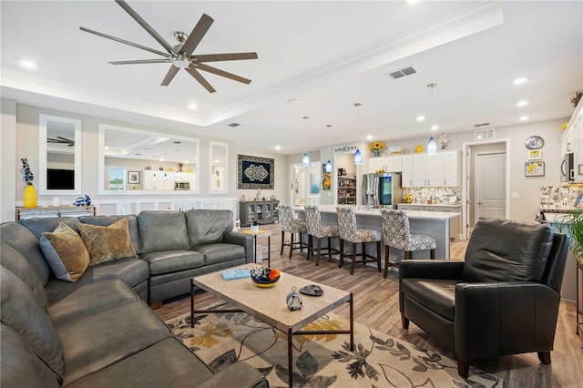 living room featuring a raised ceiling, ornamental molding, ceiling fan, and light hardwood / wood-style flooring