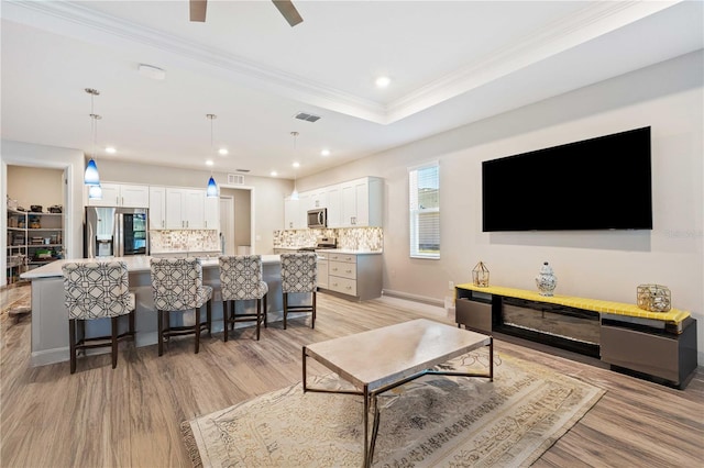 living room with crown molding, light hardwood / wood-style floors, and a tray ceiling