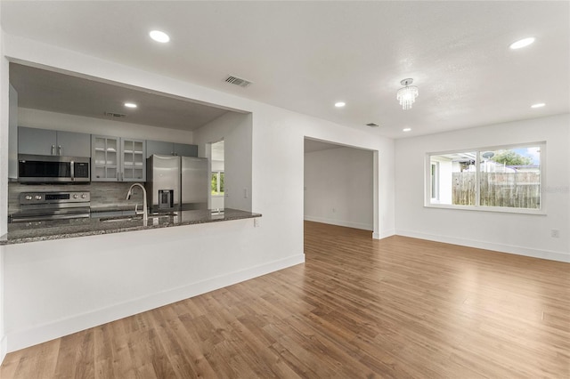 kitchen with dark stone countertops, kitchen peninsula, stainless steel appliances, wood-type flooring, and sink