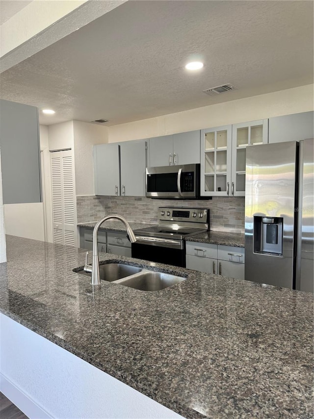 kitchen featuring a textured ceiling, sink, stainless steel appliances, backsplash, and dark stone countertops