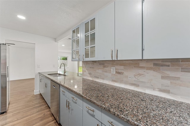 kitchen with dark stone counters, light hardwood / wood-style floors, sink, decorative backsplash, and stainless steel appliances