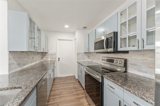 kitchen with dark stone counters, stainless steel appliances, light wood-type flooring, and tasteful backsplash