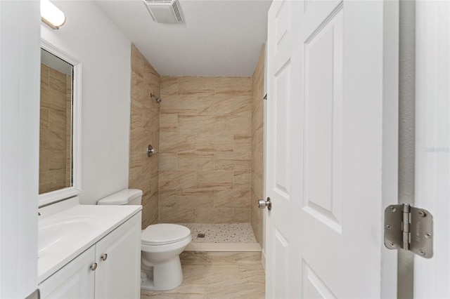 bathroom with a tile shower, vanity, and toilet