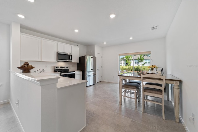 kitchen with white cabinetry, stainless steel appliances, kitchen peninsula, decorative backsplash, and light tile patterned floors