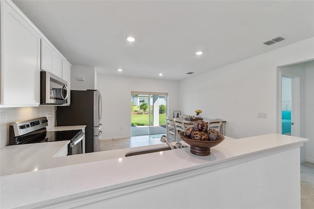 kitchen with kitchen peninsula, decorative backsplash, white cabinets, and appliances with stainless steel finishes