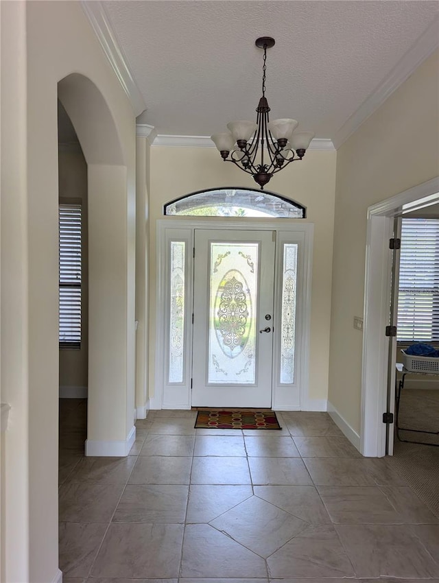 tiled entrance foyer with a textured ceiling, a healthy amount of sunlight, crown molding, and a notable chandelier