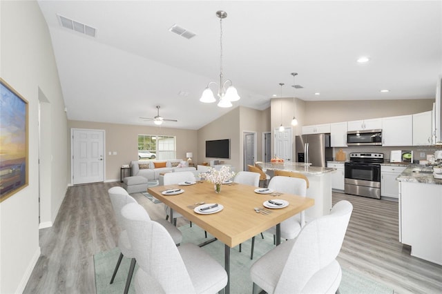 dining space featuring light wood-type flooring, ceiling fan with notable chandelier, and lofted ceiling