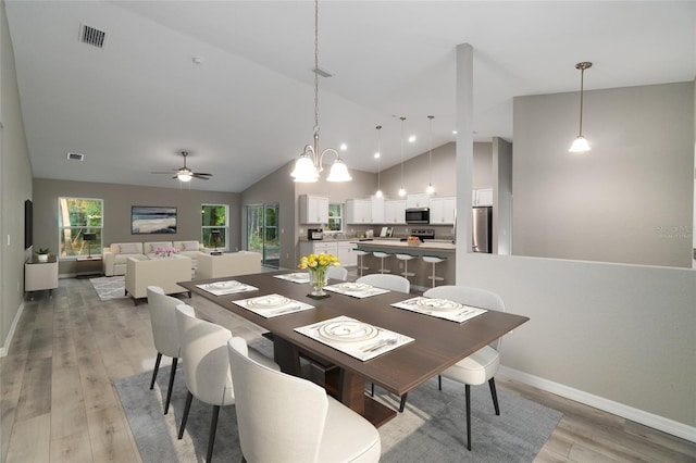 dining space featuring light hardwood / wood-style floors, ceiling fan with notable chandelier, and lofted ceiling