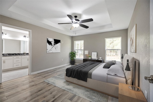 bedroom with ceiling fan, light hardwood / wood-style flooring, ensuite bathroom, and a tray ceiling