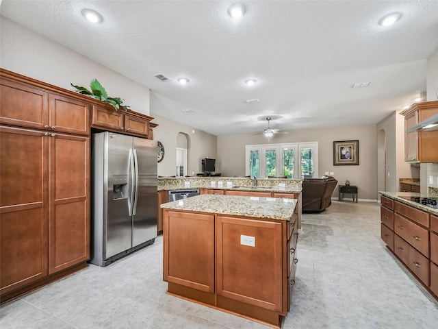 kitchen featuring ceiling fan, appliances with stainless steel finishes, light stone counters, a kitchen island, and kitchen peninsula