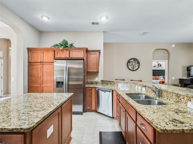 kitchen with sink, light tile patterned floors, stainless steel appliances, light stone countertops, and a textured ceiling