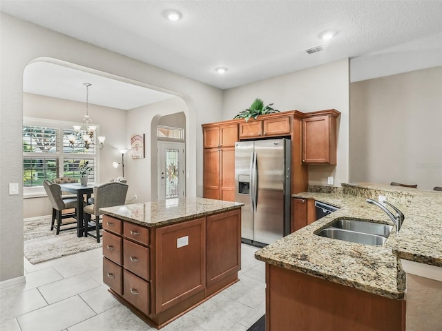 kitchen with sink, stainless steel fridge, light stone counters, decorative light fixtures, and kitchen peninsula