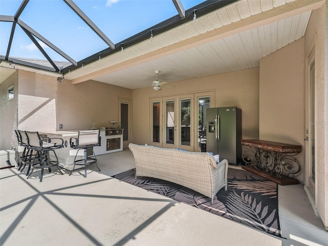 view of patio / terrace featuring an outdoor kitchen, ceiling fan, and glass enclosure